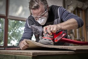 Person schleift Holz mit einem Schwingschleifer.